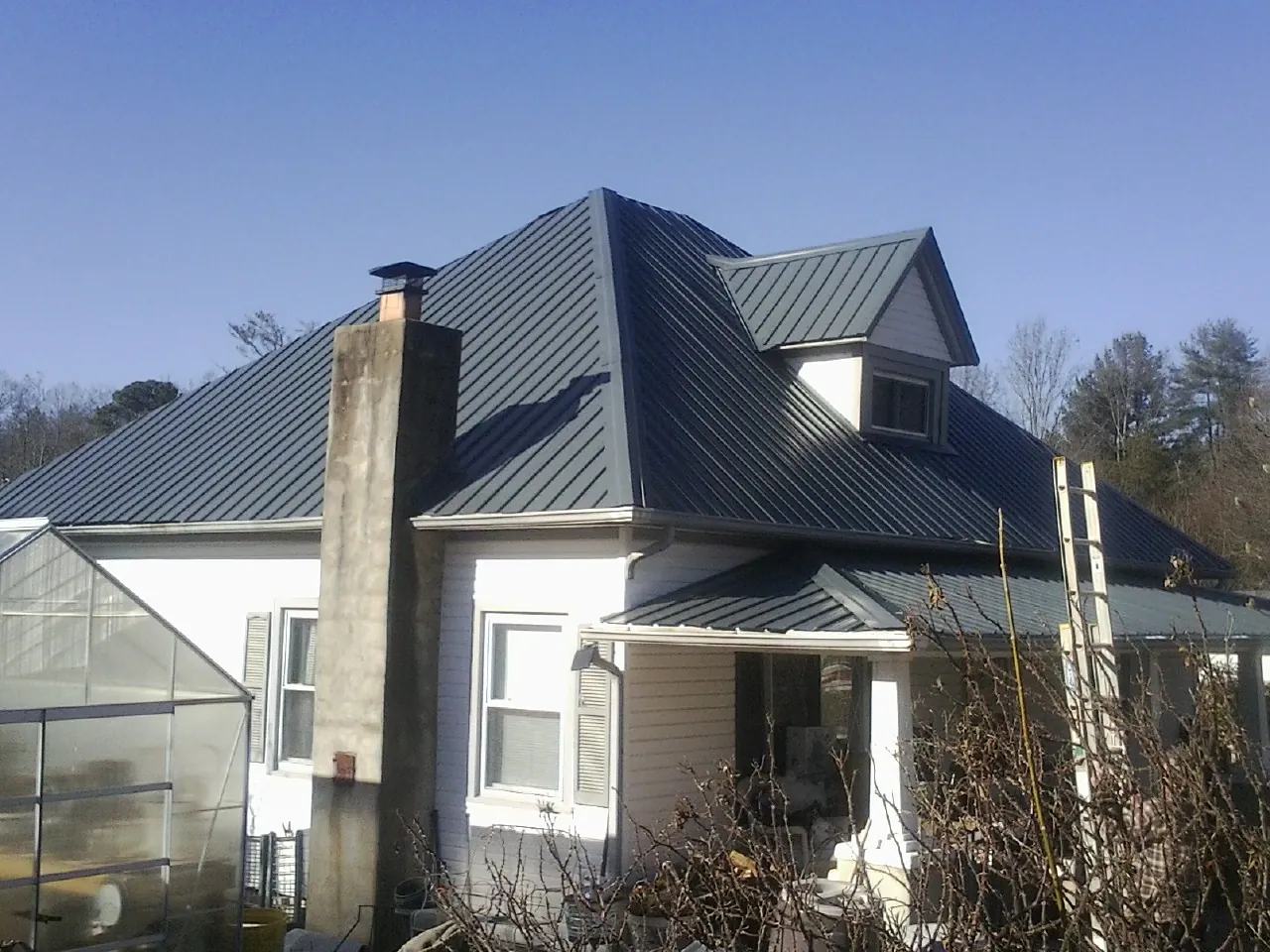 Dark blue standing seam metal roof on a white farmhouse with dormer — Slate & Tile Roof Repair by Roofing Brothers in Blue Grass