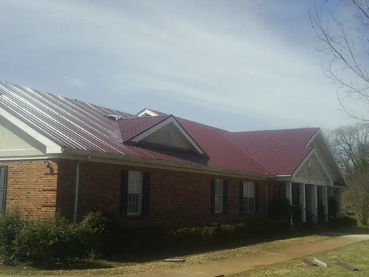 Red metal roof with gabled entries on a long brick building, from a Hail Damage Roof Repair job in Blue Grass