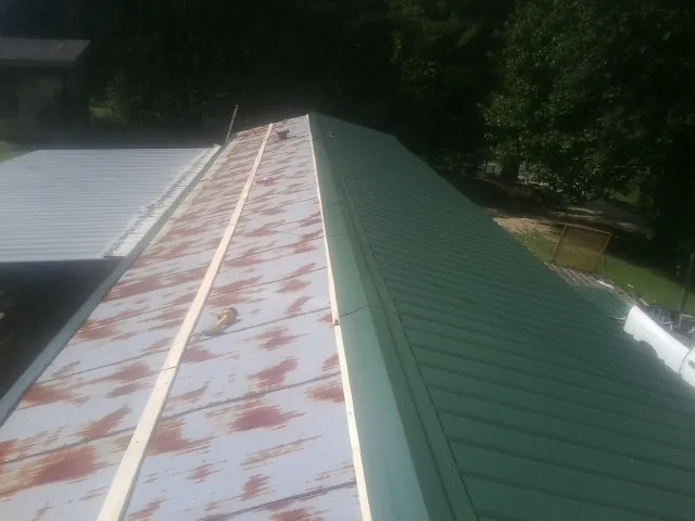Old rusted panels beside newly installed green metal roofing — Wind Damage Roof Repair by Roofing Brothers in Blue Grass