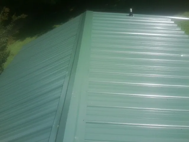 New green metal panels meeting at the ridge of a roof — Flat Roof Repair work by our crew in Blue Grass