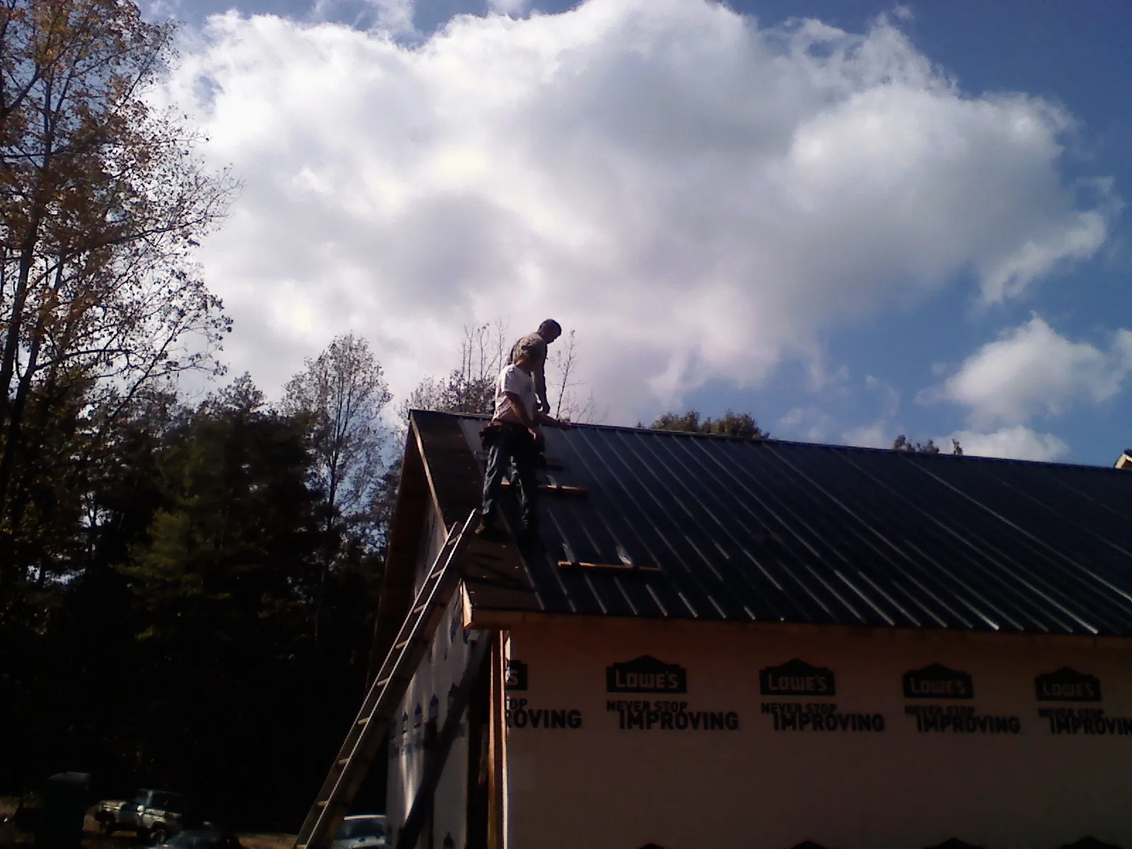 Roofer fastening dark metal panels high against a cloudy sky, from a Roof Inspection job in Blue Grass