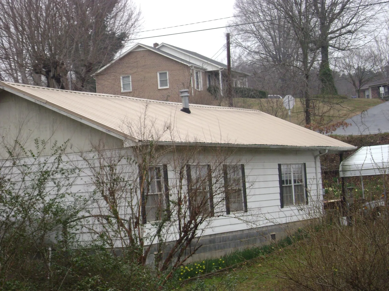 Tan metal roof on a white sided house set into a hillside — Commercial Roofing by Roofing Brothers in Blue Grass