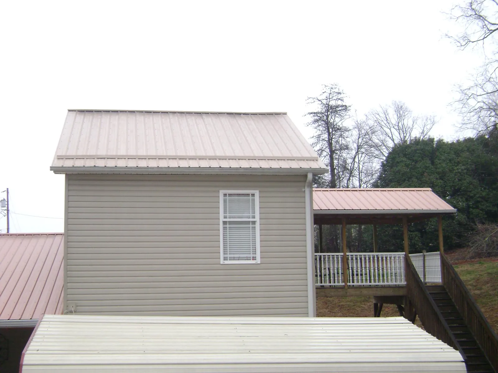 Tan metal roofs on a two story addition and attached porch, from a Roof Replacement job in Blue Grass